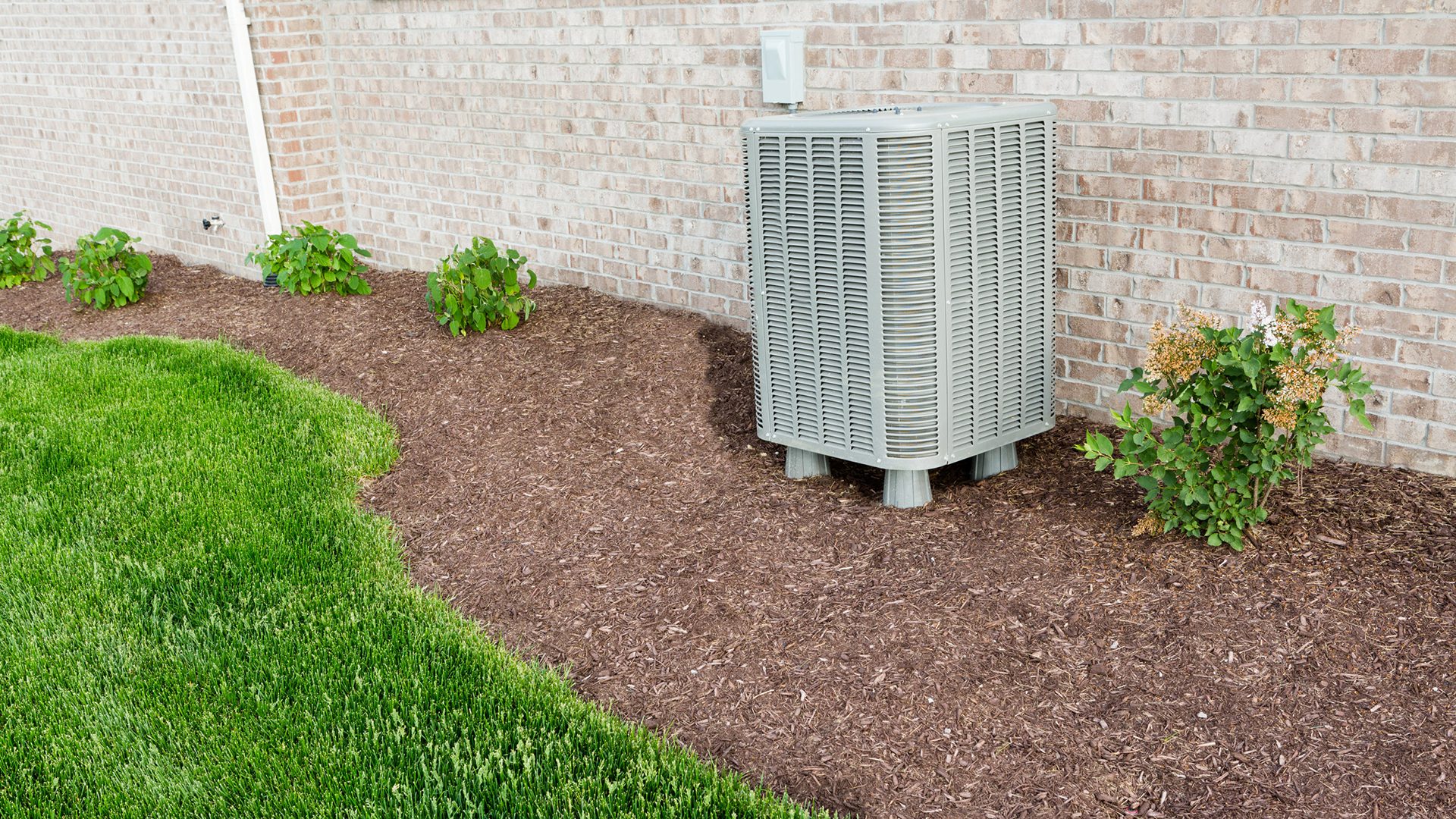 Air conditioner condenser unit standing outdoors in a garden in a neat clean mulched flowerbed for easy access for maintenance